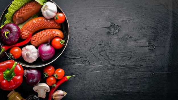 Saucisses grillées dans une casserole avec des légumes frais En bois sur la surface noire Vue de dessus