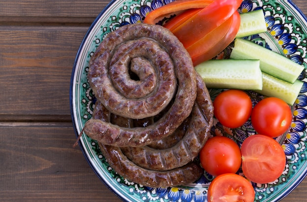 Saucisses grillées avec des légumes frais sur une table en bois.