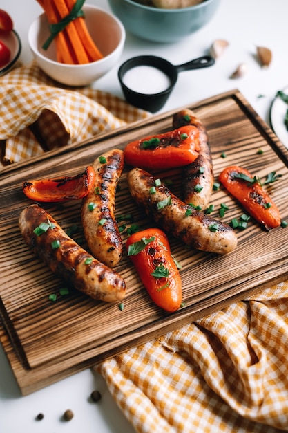 Saucisses grillées et poivrons sur une planche de bois.