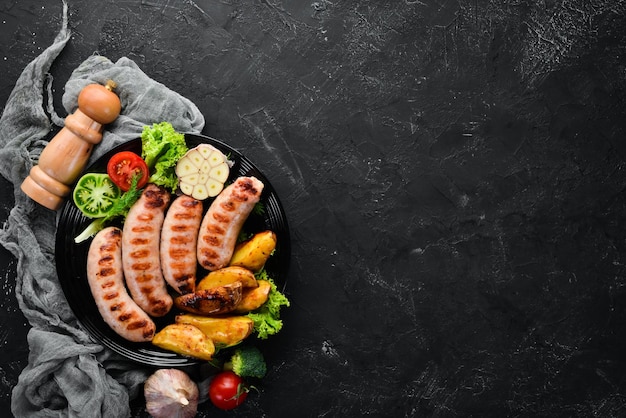 Saucisses grillées avec pommes de terre et légumes sur fond de pierre noire Viande Vue de dessus Espace de copie gratuit