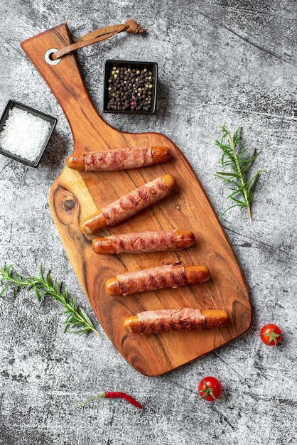 Saucisses sur une planche de bois avec un bol d'herbes et un petit bol de sel.