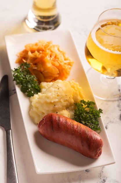 Saucisses et pommes de terre grillées avec un verre de bière sur la surface blanche