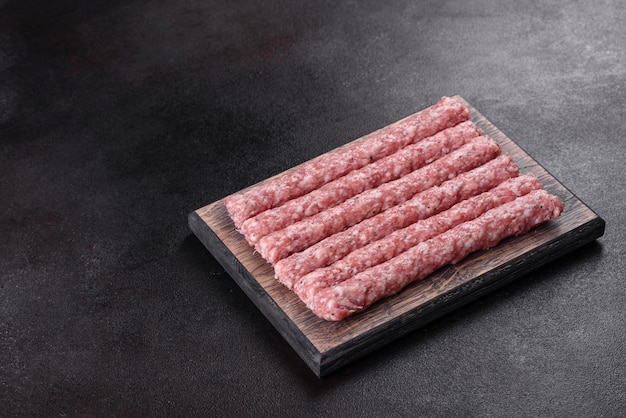 Saucisses de porc cru frais avec des épices sur une planche à découper en bois sur béton