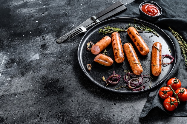 Saucisses de poulet frit avec oignon, ail et romarin. Fond noir