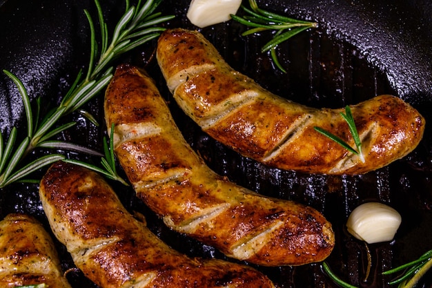 Saucisses rôties avec des brindilles de romarin et de l'ail dans une poêle à griller en fonte