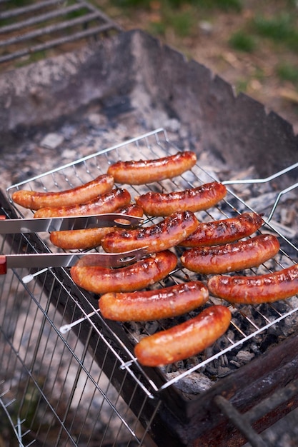 Saucisses savoureuses grillant sur la grille de gril de charbon de bois