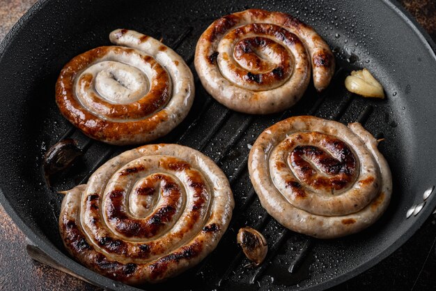 Saucisses en spirale de viande de porc bavaroise frite dans une poêle en fonte, sur le vieux fond rustique foncé