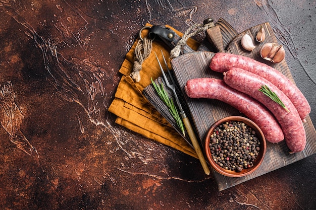 Saucisses de viande crue Bratwurst sur planche de bois avec des épices Fond sombre Vue de dessus Espace de copie