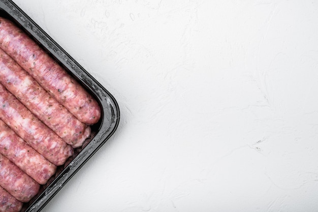 Saucisses de viande non cuites dans un emballage en plastique, sur fond de table en pierre blanche, vue de dessus à plat, avec espace de copie pour le texte