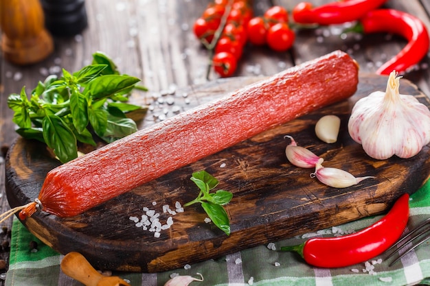 saucisson sec maison, basilic et ail, entier et en morceaux, épices et légumes sur coupe de cuisine