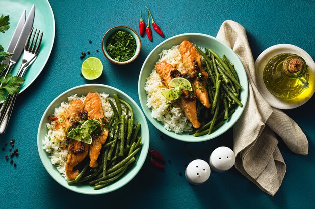 Saumon frais frit au gingembre et à l'ail dans du lait de coco, avec du riz basmati et des haricots verts dans des assiettes sur la table. recette saine pour toute la famille.