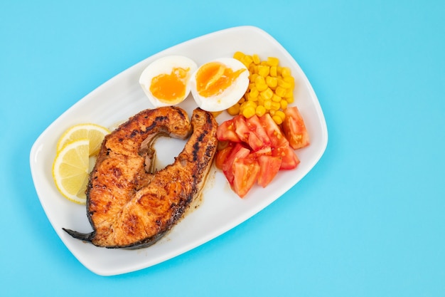 Saumon frit avec œuf à la coque, tomate et maïs sur plat blanc