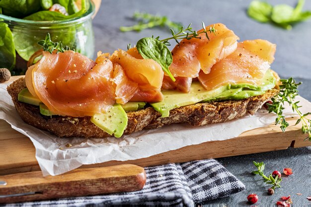 Saumon fumé appétissant et sain avec de l'avocat et des légumes (pousses d'épinards, tomates, thym) sur du pain grillé. Look fait maison.