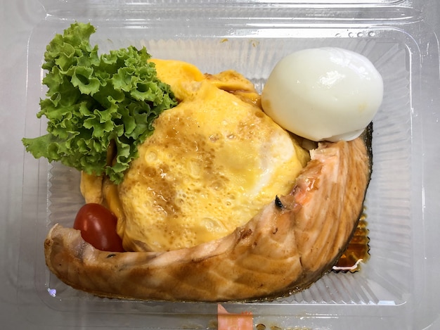 Saumon Grillé Avec Du Riz Dans Une Omelette Aux œufs Dans Le Récipient Sur La Table