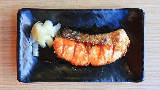 Saumon Teriyaki dans une assiette noire sur une table en bois, cuisine japonaise.