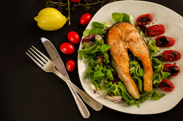 Saumon avec tomates cerises grillées et mélange de feuilles de salade et de citron