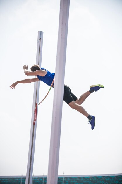 Saut à la perche un jeune homme athlétique sautant par-dessus la barre