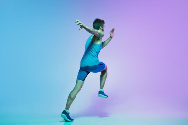 En saut Portrait de jeune homme caucasien courant jogging sur fond de studio dégradé en néon