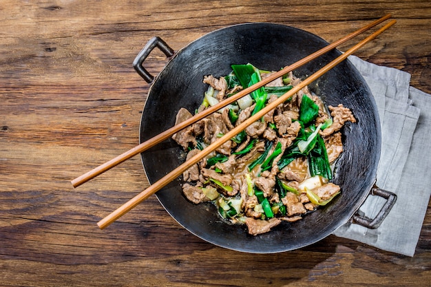 Sauté de bœuf mongol traditionnel chinois dans un wok chinois en fonte avec des baguettes de cuisine