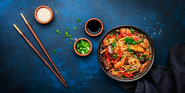 Sauté de nouilles au poulet paprika rouge champignons ciboulette et graines de sésame dans un bol plat de cuisine asiatique fond de table bleu vue de dessus