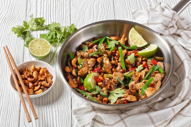 Sauté de poulet aux noix de cajou thaï dans une casserole sur une table en bois avec des baguettes et des ingrédients vue horizontale d'en haut gros plan