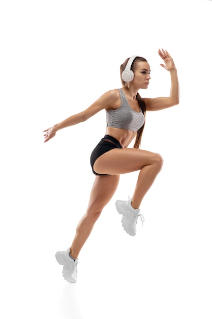 Sauter. Athlète féminine professionnelle caucasienne, entraînement de coureur isolé sur fond de studio blanc. Femme musclée et sportive. Concept d'action, mouvement, jeunesse, mode de vie sain. Copyspace pour l'annonce.