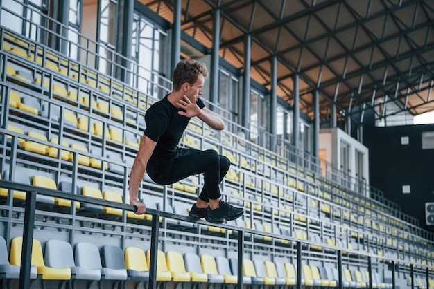 Sauter et faire du parkour sur les gradins Jeune homme sportif en chemise et pantalon noirs à l'extérieur pendant la journée