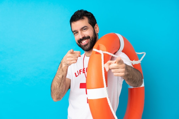 Sauveteur homme sur mur bleu isolé pointe le doigt vers vous en souriant