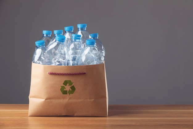 Sauvez le monde et le concept d'environnement Bouteille en plastique bleue utilisée dans un sac en carton marron sur un bureau en bois et un fond sombre Peut être utilisée pour réutiliser le concept de recyclage et d'environnement