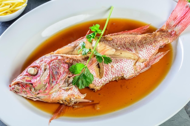 Saveurs de la mer Gros plan de poisson vivaneau rouge entier cuit dans de la sauce soja au gingembre sur une assiette en 4K