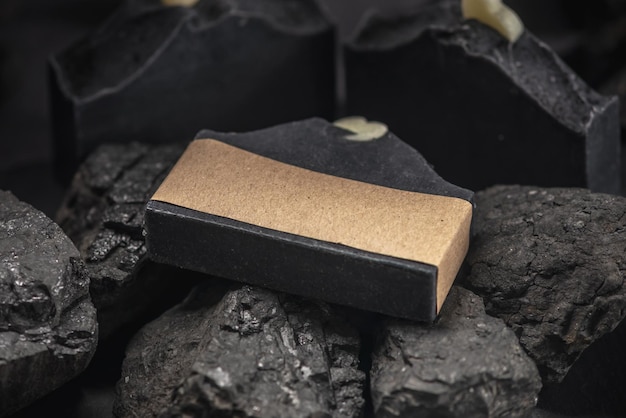 Savon au charbon de bois naturel enveloppé de papier kraft sur des charbons sur fond noir Concept de fabrication et d'utilisation de savon et de cosmétiques bio cadeaux écologiques faits à la main
