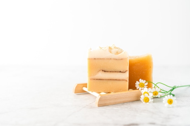 Savon maison aux fleurs de camomille dans un porte-savon en bois sur fond de marbre blanc zéro déchet