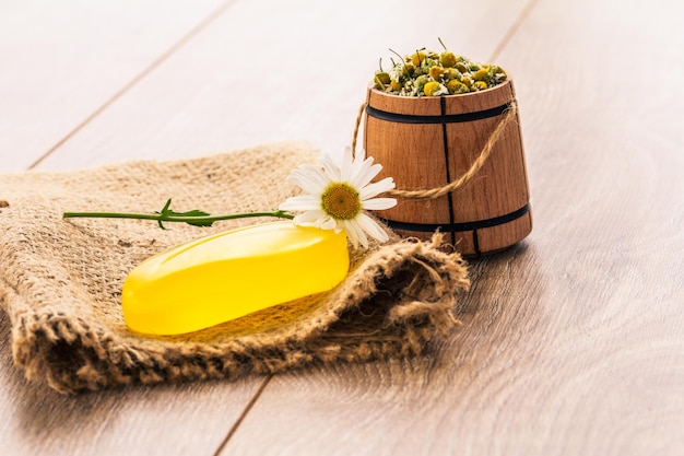 Savon sur un sac avec une camomille fraîche et un petit tonneau en bois avec du thé à la camomille en vrac