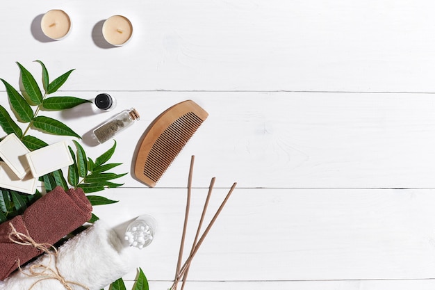 Savons naturels faits à la main avec des bougies à l'huile, une serviette brune et des feuilles vertes sur fond de bois blanc