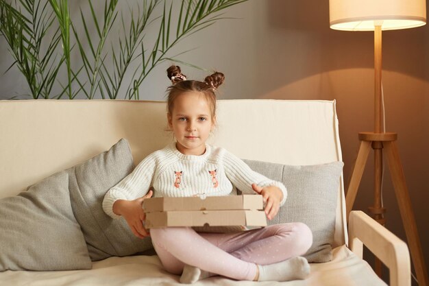 Savoureuse collation de restauration rapide Mignonne petite fille assise sur un canapé tenant une boîte à la maison repas délicieux enfant portant