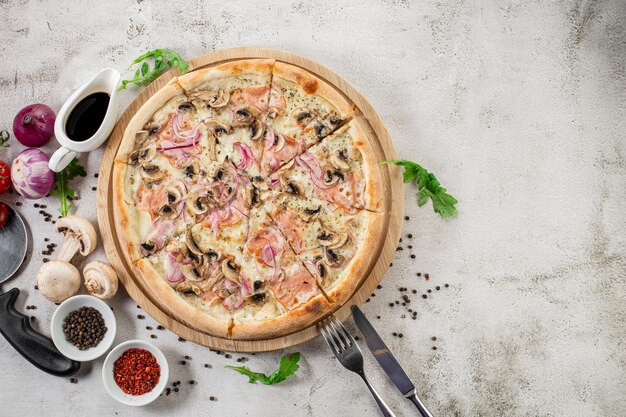 Savoureuse pizza au jambon, champignons et oignon sur fond de béton