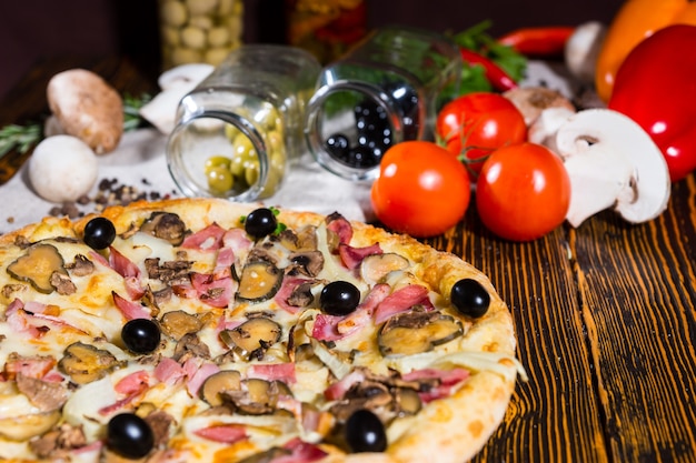 Savoureuse pizza aux olives noires sur table en bois, tomates, champignons et autres légumes