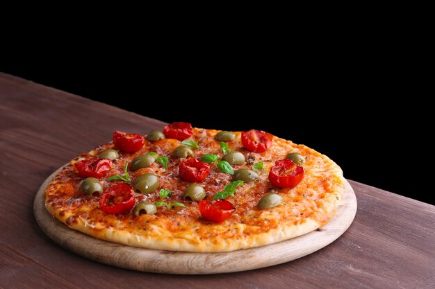 Savoureuse pizza aux tomates cerises, olives vertes et herbes sur table en bois sur fond noir