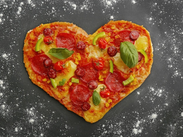 Savoureuse pizza en forme de coeur sur une table en poudre de farine noire