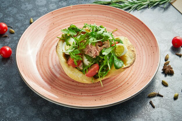 Savoureuse salade niçoise servie en pita dans un bol rose sur une surface sombre avec des ingrédients