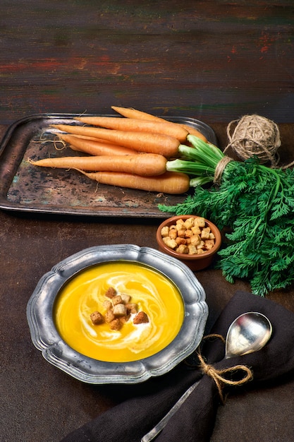 Savoureuse soupe végétarienne aux carottes servie avec des croûtons à la crème et un arc en étain métallique