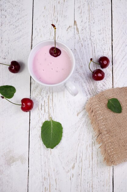 Savoureuses belles crêpes dans une assiette blanche avec cerise et yaourt dans une tasse en verre sur une table en bois clair avec des feuilles de menthe.