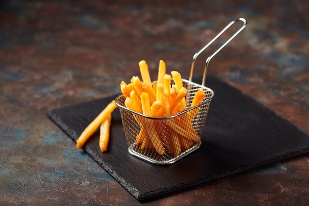 Photo savoureuses frites dans un panier en fer sur une planche à découper en ardoise