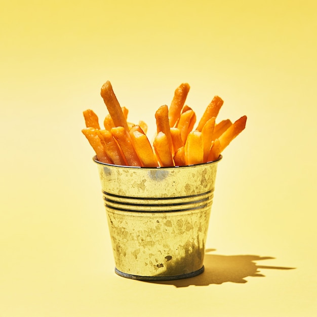 Savoureuses frites dans un seau en métal sur une table jaune au soleil.