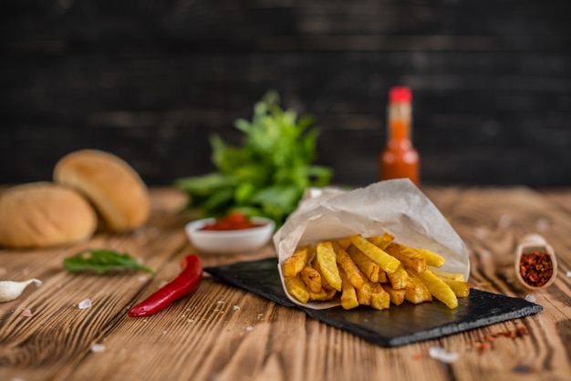 Savoureuses frites avec des légumes sur un fond sombre. Fast food. Il peut être utilisé comme arrière-plan