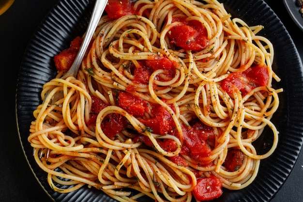 Savoureuses pâtes italiennes classiques avec sauce tomate et fromage sur assiette sur fond sombre. Vue de dessus.