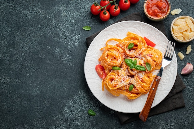 Savoureuses pâtes tagliatelles italiennes classiques appétissantes avec sauce tomate, fromage parmesan et basilic sur une assiette sur une table sombre. Vue de dessus, horizontale. Vue de dessus avec espace de copie.