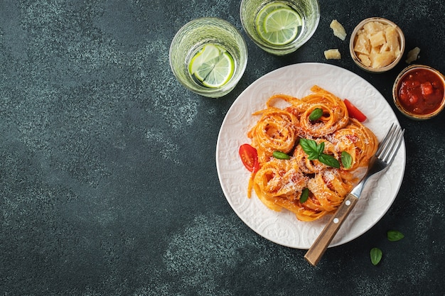 Savoureuses pâtes tagliatelles italiennes classiques appétissantes avec sauce tomate, fromage parmesan et basilic sur une assiette sur une table sombre. Vue de dessus, horizontale. Vue de dessus avec espace de copie.