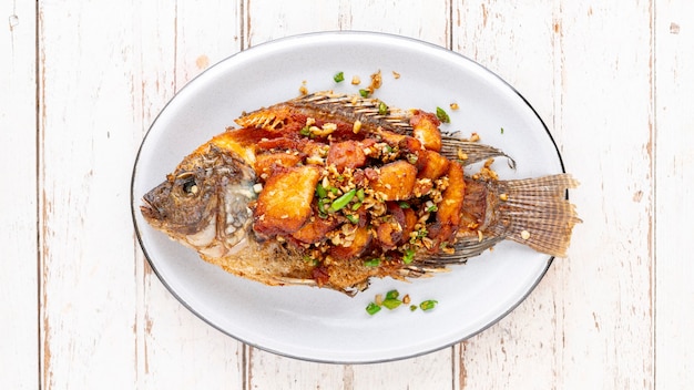 Savoureux grand poisson tilapia du Nil frit avec piment et ail dans une assiette ovale en céramique sur fond de texture en bois blanc, vue de dessus, rapport Full HD, 16 x 9