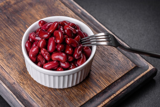 Savoureux haricots rouges en conserve dans un beau bol blanc sur une planche de bois